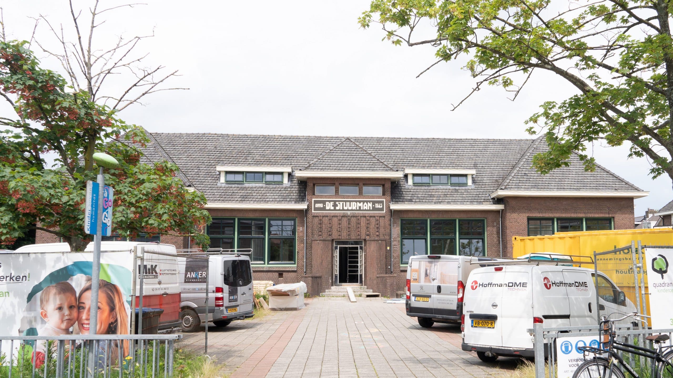 Een groot bakstenen school in renovatie, met een de nieuwe naam op het bord boven de ingang: ‘DE STUURMAN’. Voor de oude school, op het voormalige speelterrein liggen bouwmaterialen en staan werkbussen. Foto is genomen vanaf de ingang op de Oranjelaan.