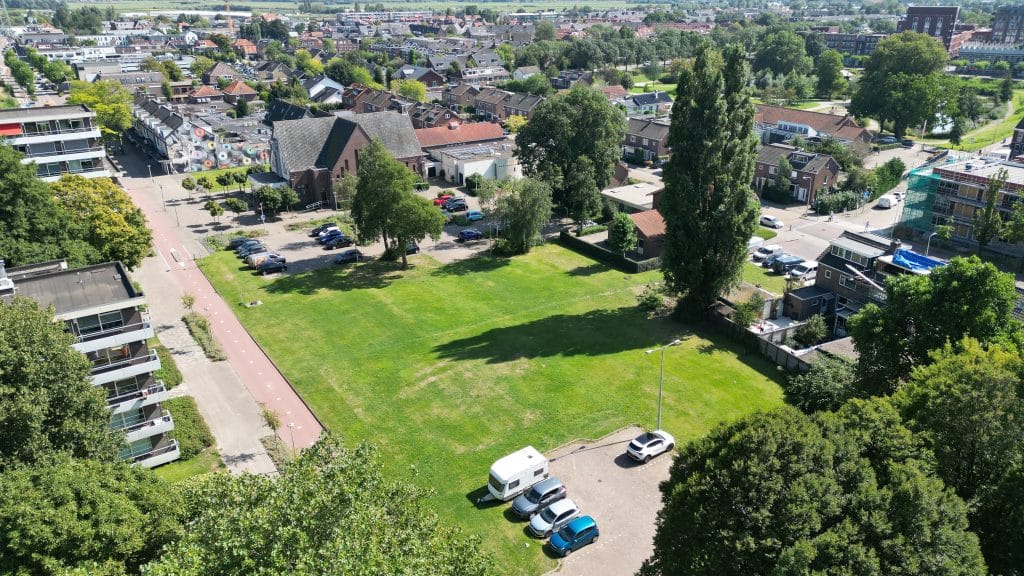 Dit is een dronefoto. Op de foto is een deel van de parkeerplaats en een groot grasvlak te zien op de Passage. Hier stond vroeger de Oude Spijsfabriek en hier komt in de toekomst een appartementencomplex. Op de achterkant is het Sleutelkwartier te zien