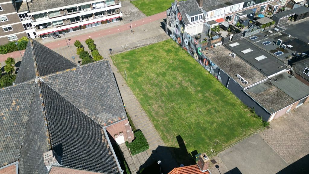 Dit is een drone-foto. Op de foto is een grasvlakte te zien naast het muziekgebouw op de Passage. Hier stond vroeger de Oude Pastorie en hier komen in de toekomst woningen.