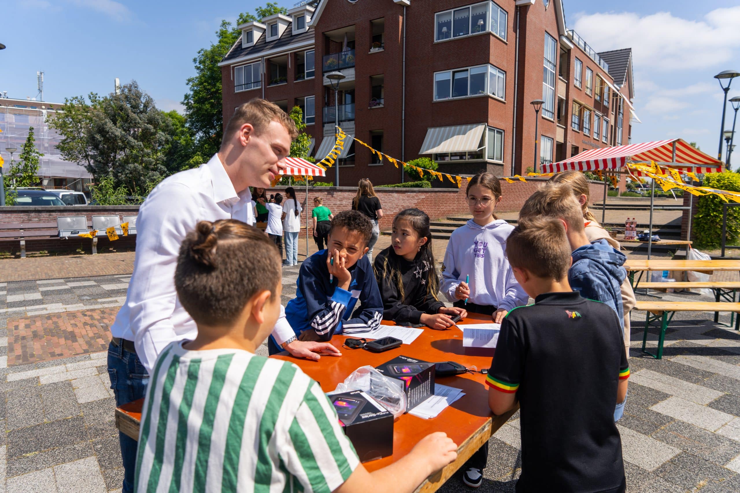 Projectleider Jard van der Heijden staat om een tafel met een groep kinderen. Er is een markt opgebouwd die geplaatst is bij het Raadhuisplein