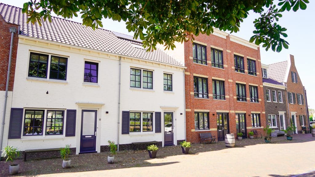 Een foto van de nieuwe moderne huizen op de Nesse nummer 24-34. De voorkanten van de huizen zijn verschillend opgebouwd, waarbij de ene donker en de ander licht zijn. Er staan plantenbakken voor de deur.