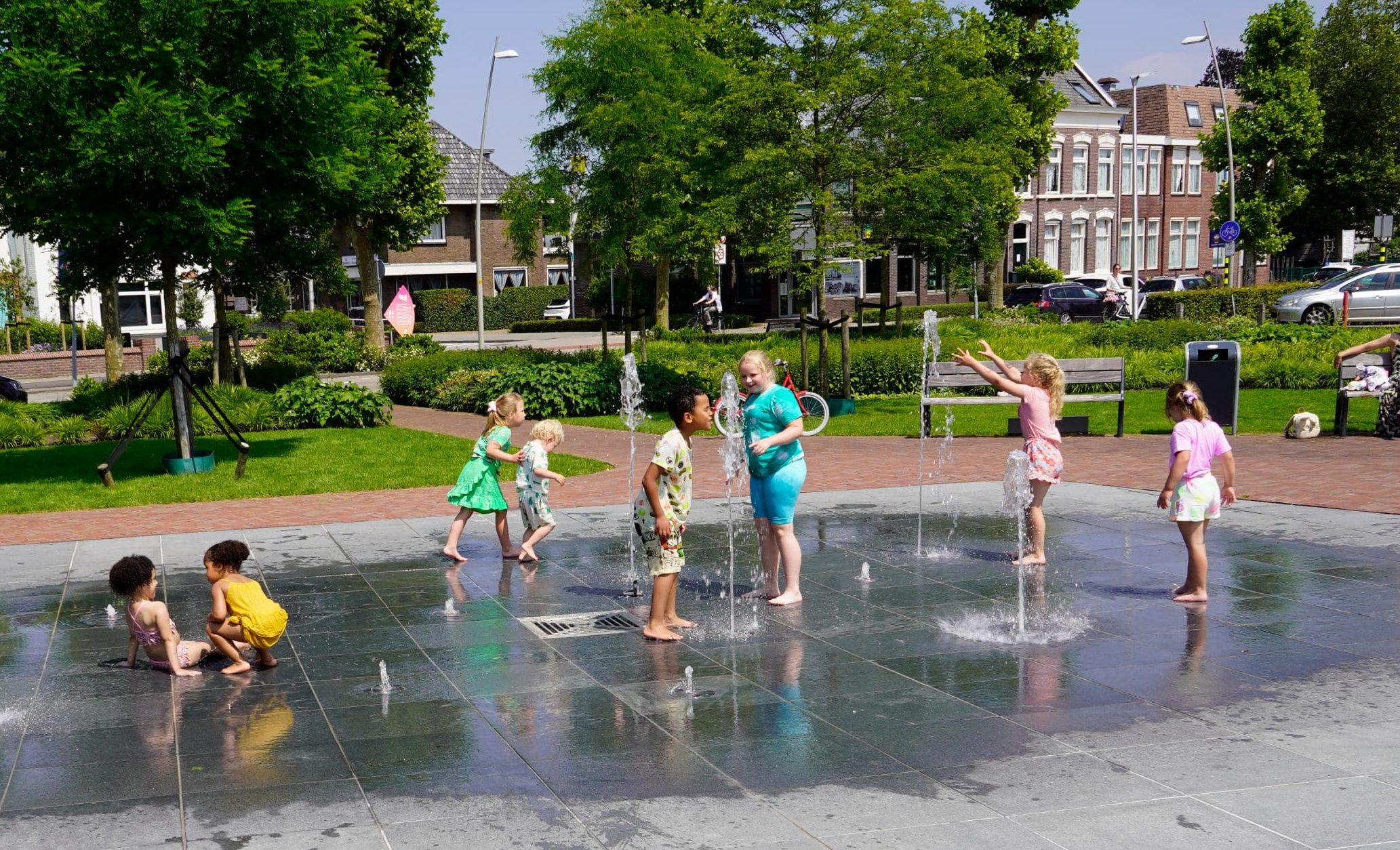 Spelende kinderen tussen de waterfonteintjes in het Beukenhofpark voor het gemeentehuis. Op de achtergrond is de Kerkweg-oost te zien. 