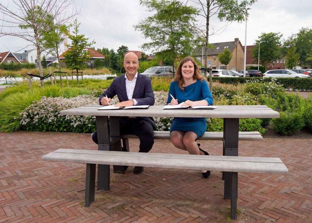 Wethouder Femke Vleij en ontwikkelaar Tomas van den Berg ondertekenen de koopovereenkomst. Zij zitten op een bankje in het Beukenhofpark.