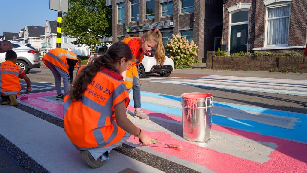 Kinderen die het zebrapad voor de Theo Thijssenschool aan het verven zijn met kwasten en rollers.