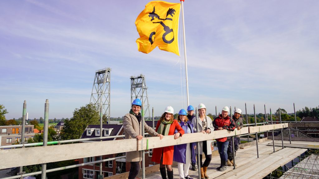 Viering van het hoogste punt van het Raadhuisplein. Wethouder Femke Vleij staat met vertegenwoordigers van Woonpartners en BM van Houwelingen op het dak. Op de achtergrond is de hefbrug te zien.