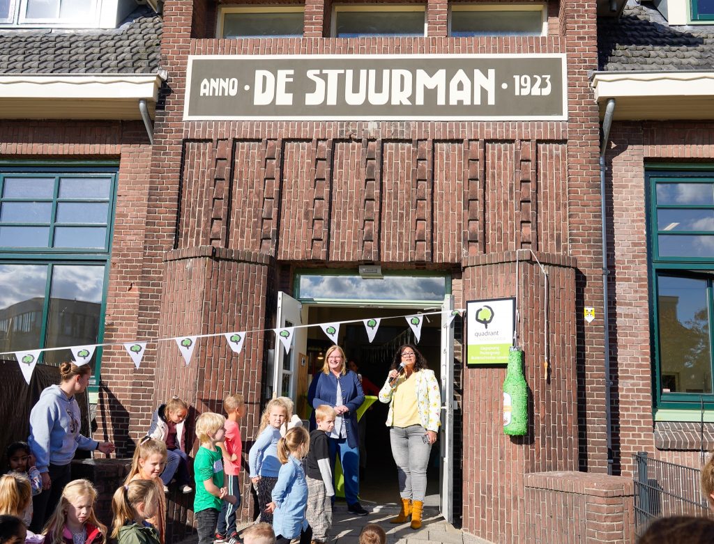 Wethouder Brigitte Leferink deed de opening van de buitenschoolse opvang. Hier zijn veel kinderen bij en de vlaggetjes hangen.