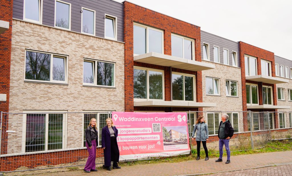 Wethouder Femke Vleij, Projectleider Tara van der Ban, Frans en Tamara Vink voor het bouwhekdoek van Waddinxveen Centraal. Deze hangt voor het gebouw. 