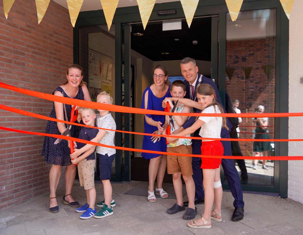 De burgemeester knipt linten door met een aantal kinderen bij de ingang van het nieuwe gezondheidscentrum