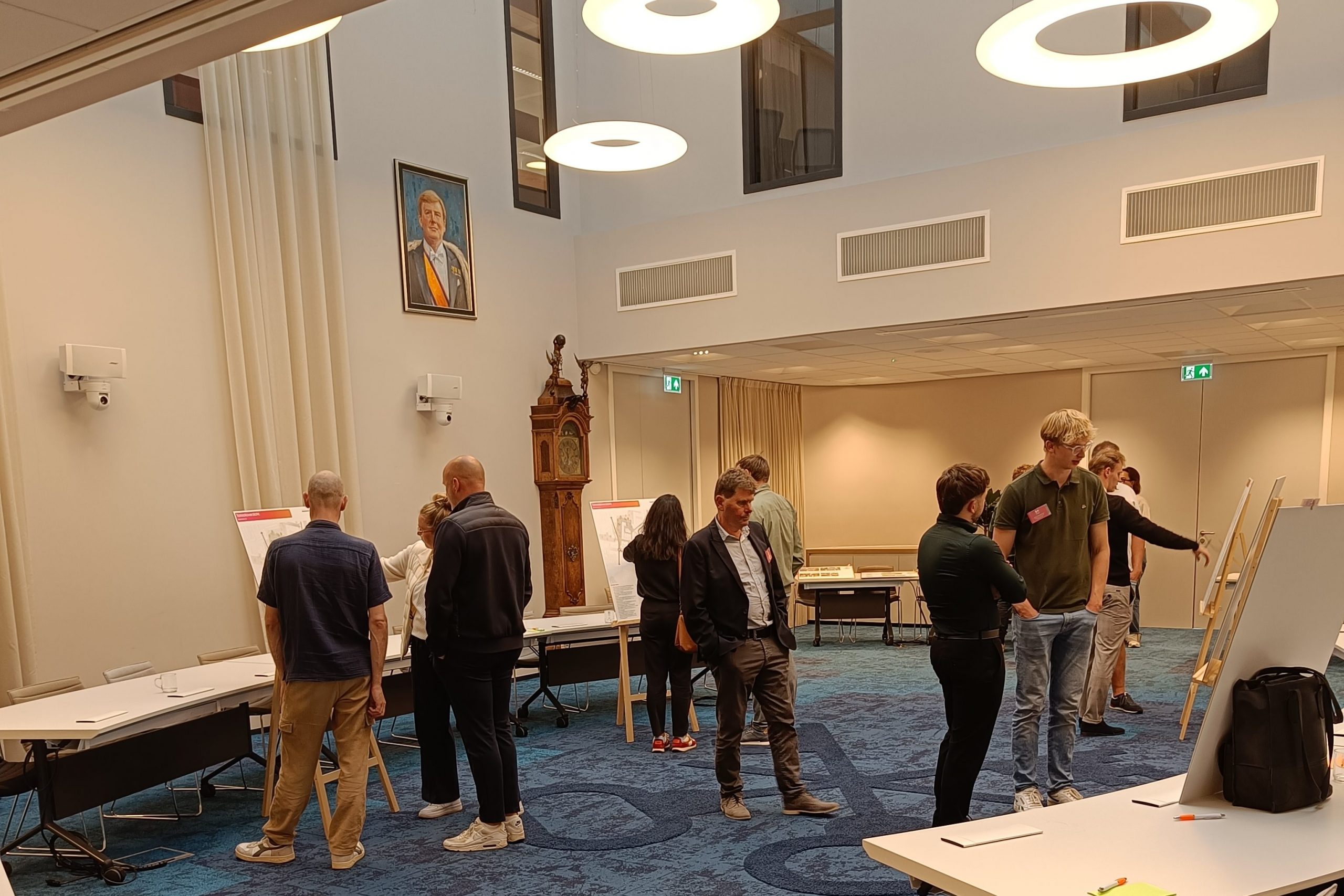 Overzichtsfoto informatiebijeenkomst. Verschillende mensen zijn zichtbaar in de raadzaal van het gemeentehuis. er staan presentatieborden.